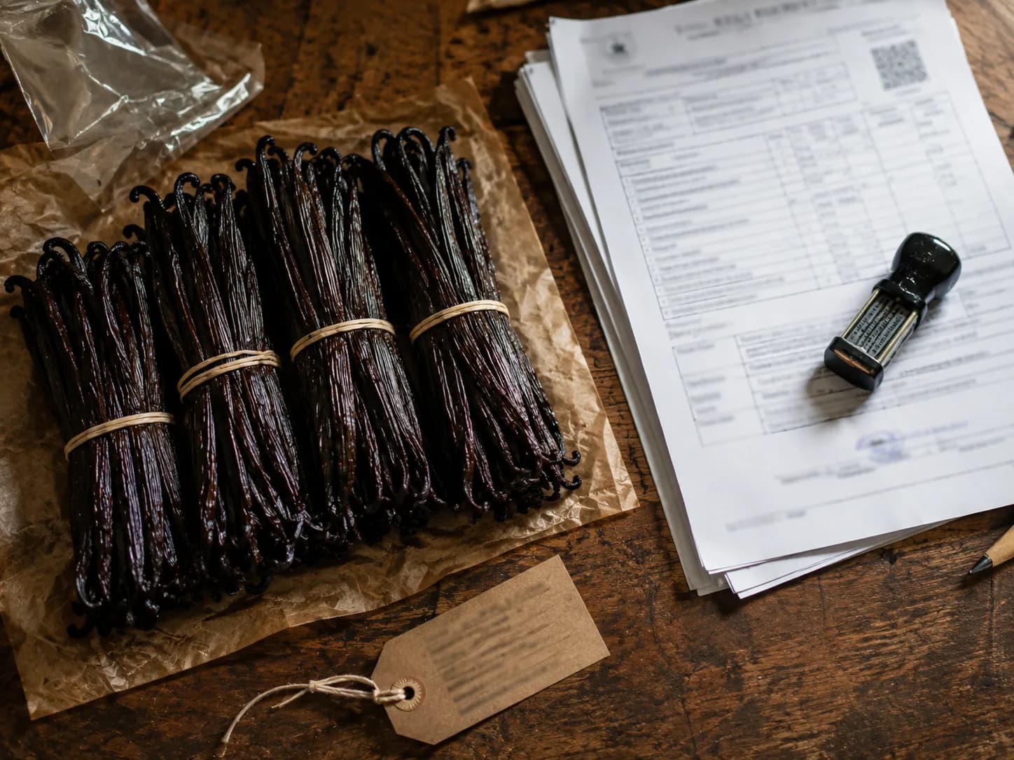 Bundled cured vanilla beans beside export paperwork and a company stamp